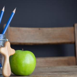 photo of school desk with pencils, apple, and a small wooden cross